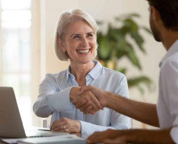 Smiling old mature saleswoman handshake businessman client customer hire job candidate at employment business meeting, happy middle aged bank manager sell loan insurance service shake customer hand