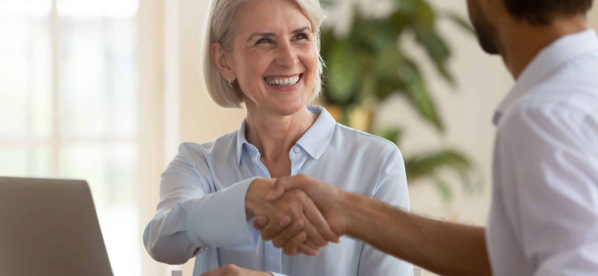 Smiling mature saleswoman handshake businessman client customer at business meeting